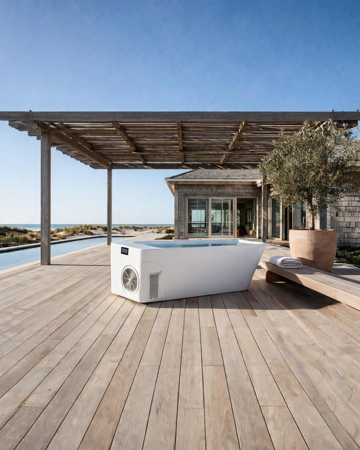 MONOLITH vessel filled with cold water on a deck under a timber pergola, a shingled house and the sea beyond