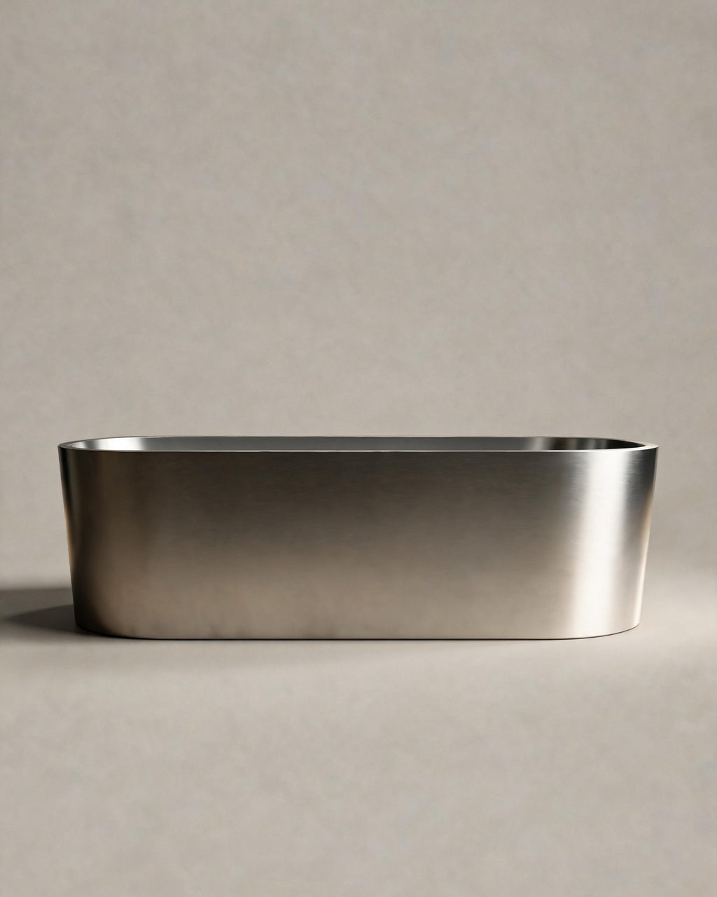 OBLONG hot and cold vessel, a long oval in Satin Steel, side view on a warm grey studio background