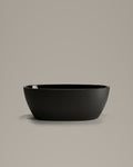 OVUM black egg-shaped vessel, side view, on a warm grey studio background