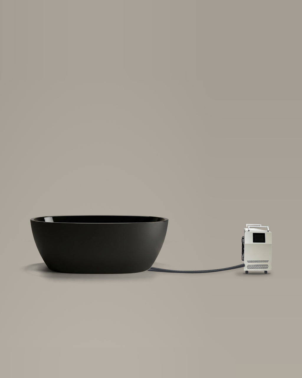 Black egg-shaped bathing vessel on a warm grey studio backdrop beside its Hot & Cold Unit, connected by two braided hoses